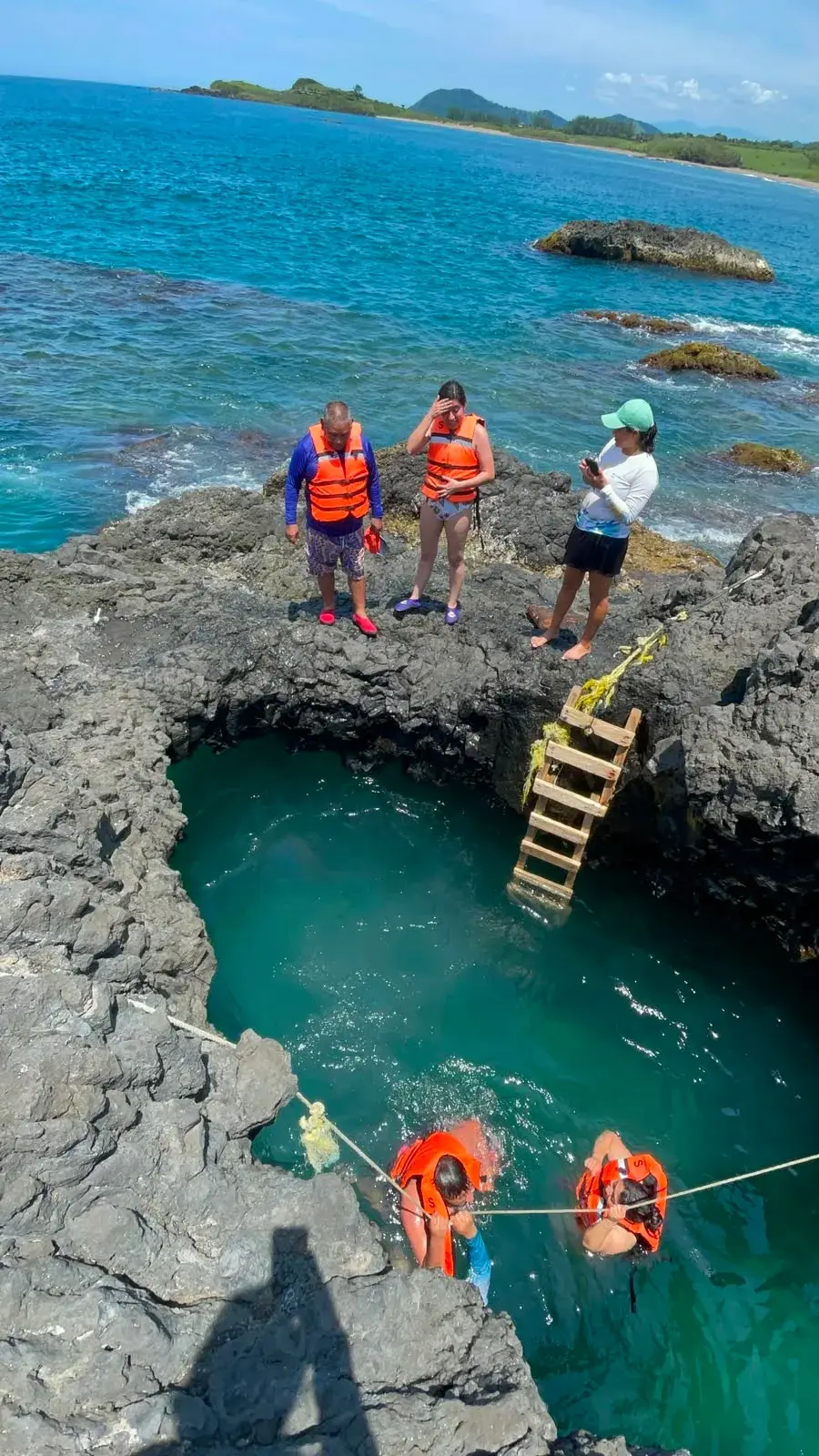 Poza de mar entre roca volcánica en Playa Ermita, con una escalera de madera y visitantes nadando, en Los Tuxtlas, Veracruz