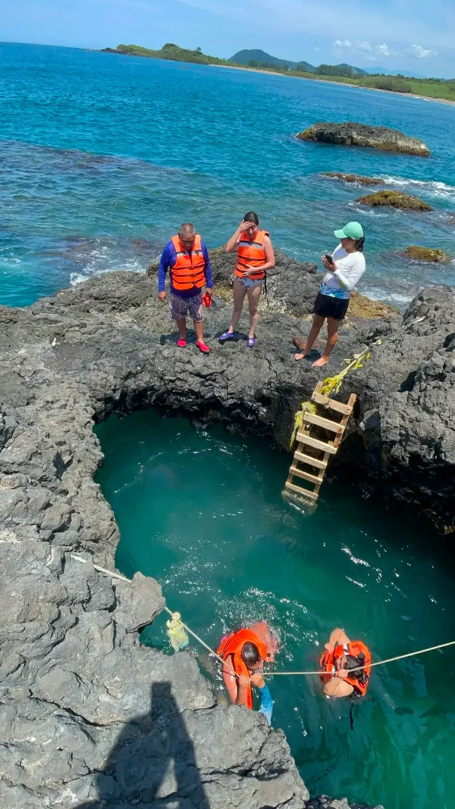 Poza de mar entre roca volcánica en Playa Ermita, con una escalera de madera y visitantes nadando, en Los Tuxtlas, Veracruz