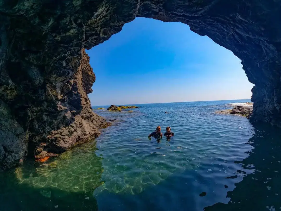Cueva de roca volcánica abierta al mar en Playa Ermita, con dos personas nadando, en Los Tuxtlas, Veracruz