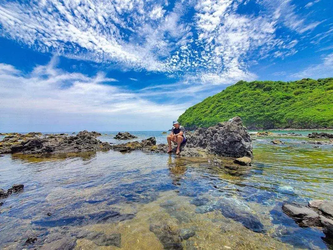 Visitante sentado sobre las rocas volcánicas de Montepío junto a una poza de agua cristalina, con el cerro verde al fondo, en Los Tuxtlas, Veracruz