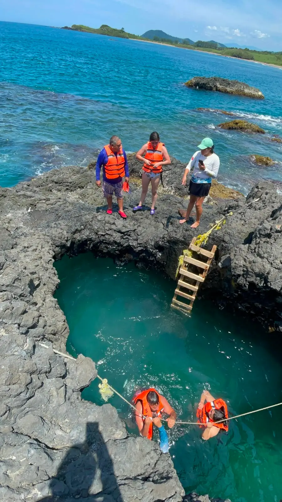 Viajeros bajando por una escalera hacia una poza natural, asistidos por el guía