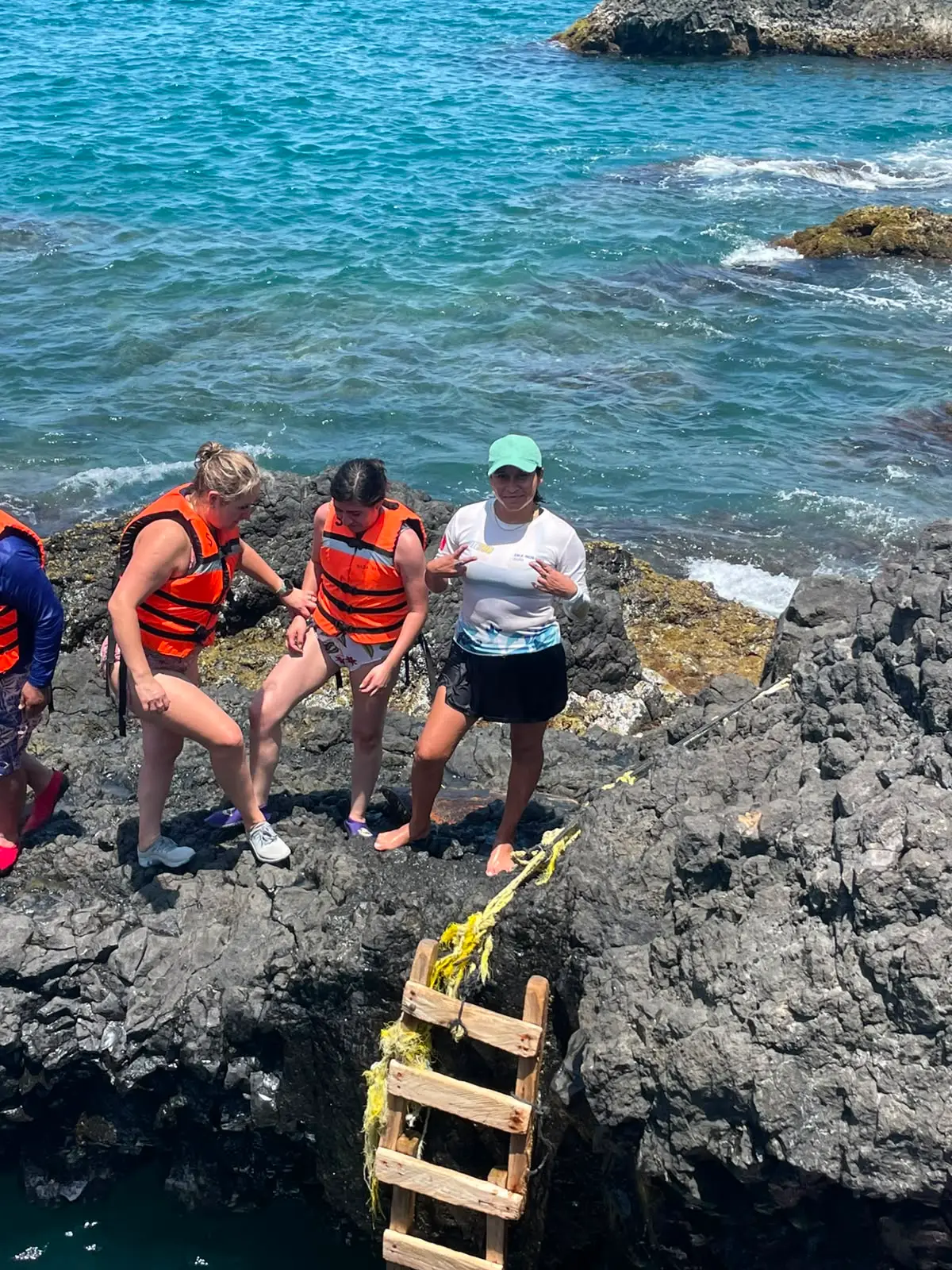 Viajeros nadando con chaleco en una poza natural de la costa, guía de BoteTur al frente