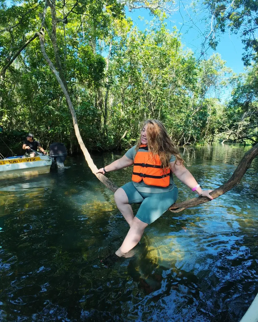 Viajera sobre una rama en aguas cristalinas entre la selva, con la lancha de BoteTur al fondo