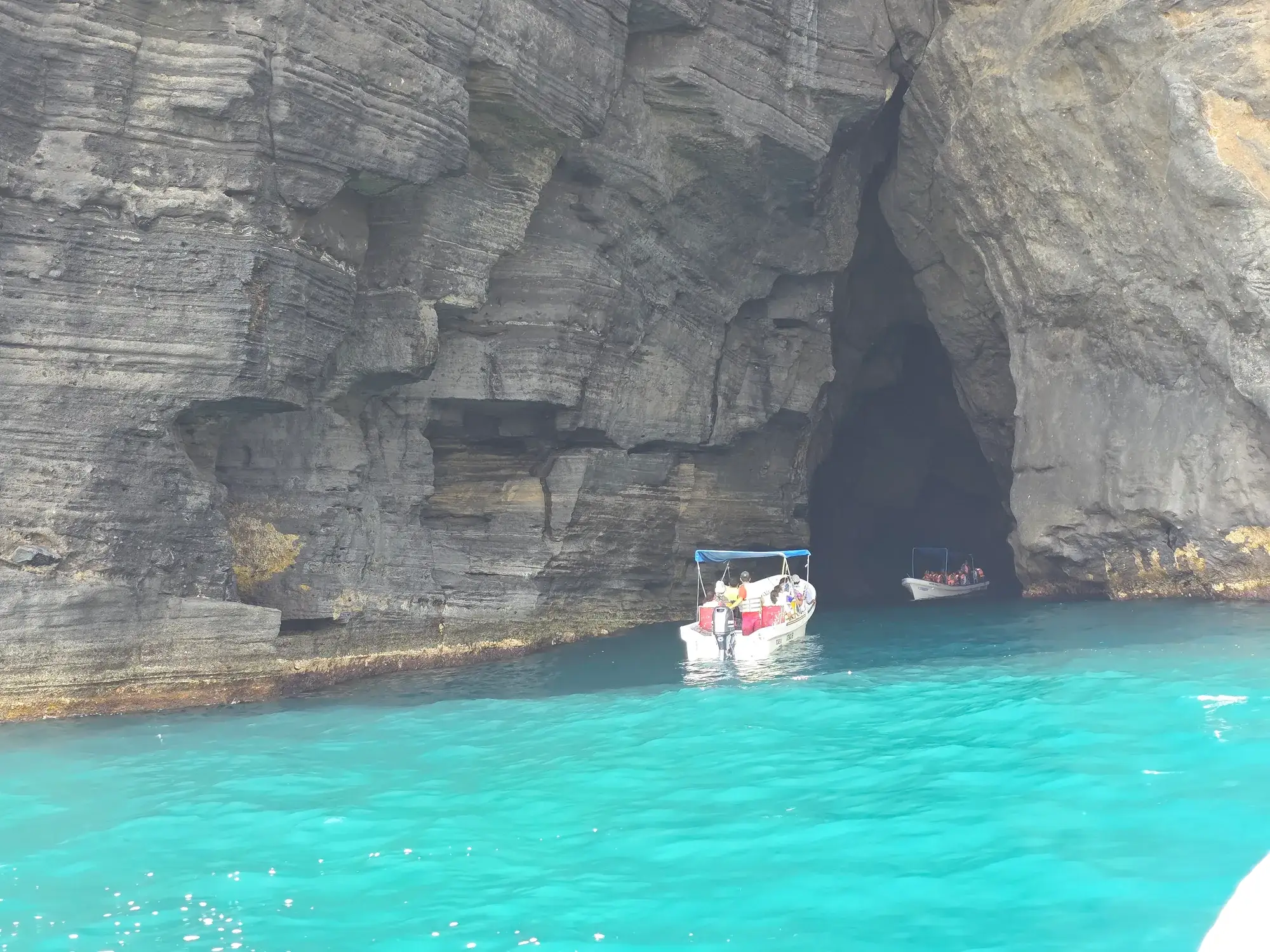 Cueva marina en los acantilados de Roca Partida, Veracruz, con lanchas de visitantes entrando por la boca sobre agua turquesa