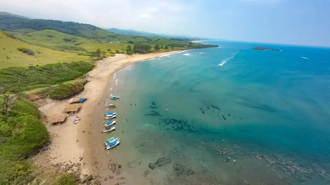 Vista aérea de la playa de Roca Partida en Los Tuxtlas: arena, lanchas en la orilla y el mar turquesa con la roca al fondo